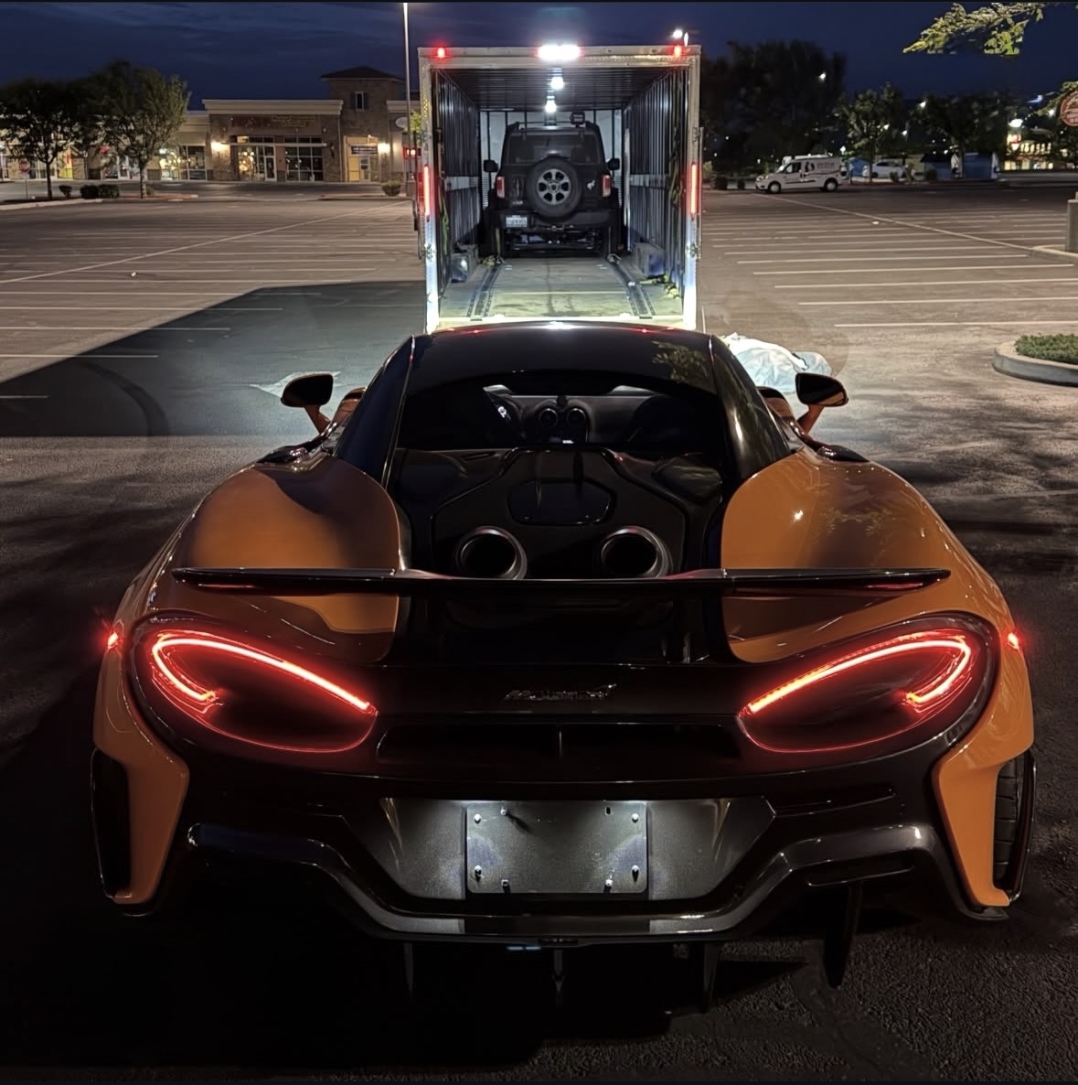 McLaren supercar parked behind an open Royalty Auto Transport enclosed trailer at night